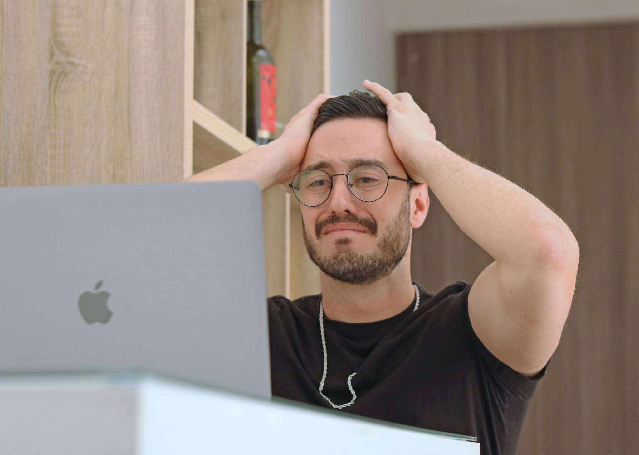 Man holding his head while looking at a laptop, illustrating emotional overwhelm and stress linked to nervous system dysregulation and the Window of Tolerance.