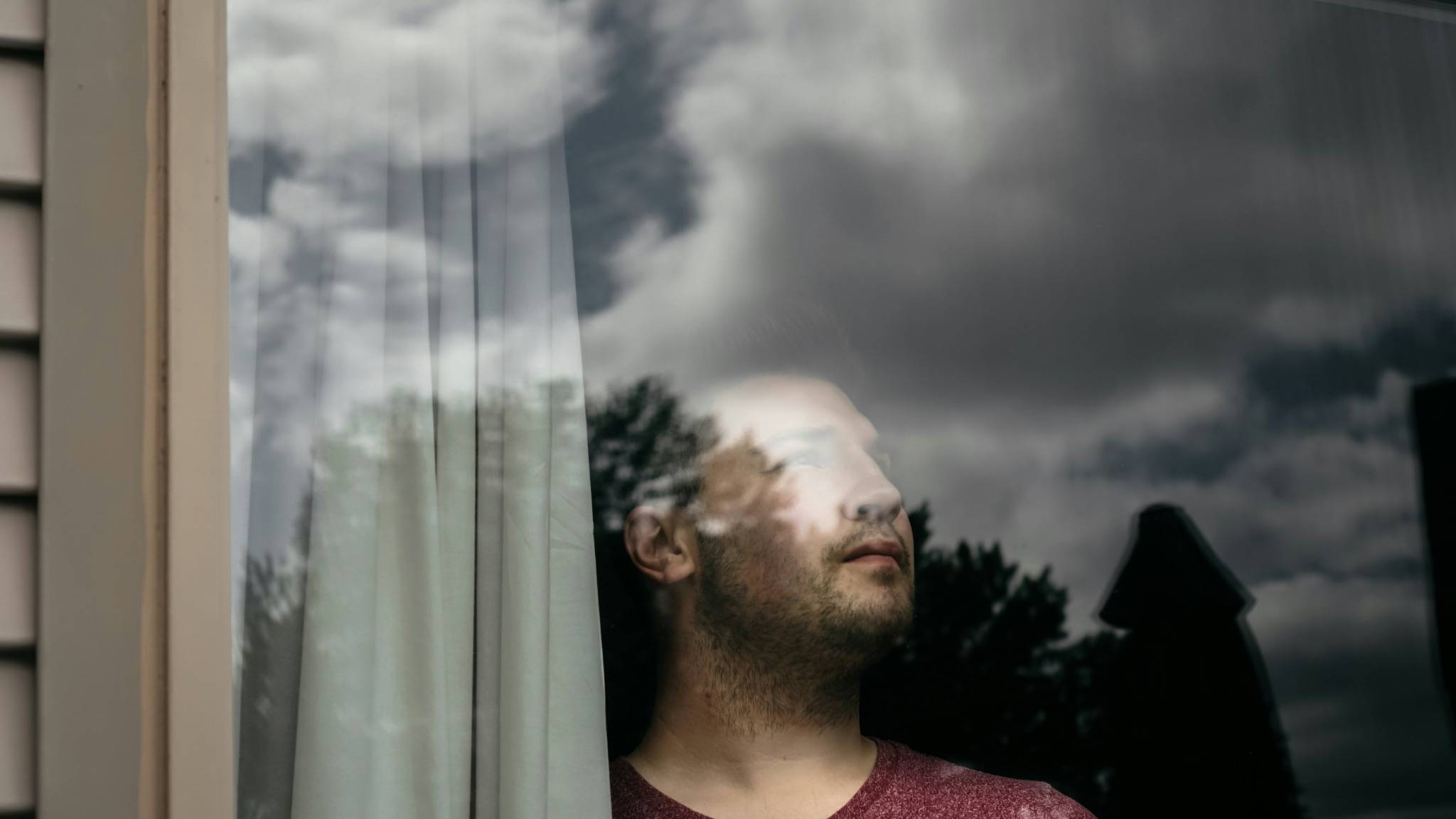 Man looking out of a window with reflection in glass, symbolising dissociation, emotional detachment, and feeling disconnected from reality.