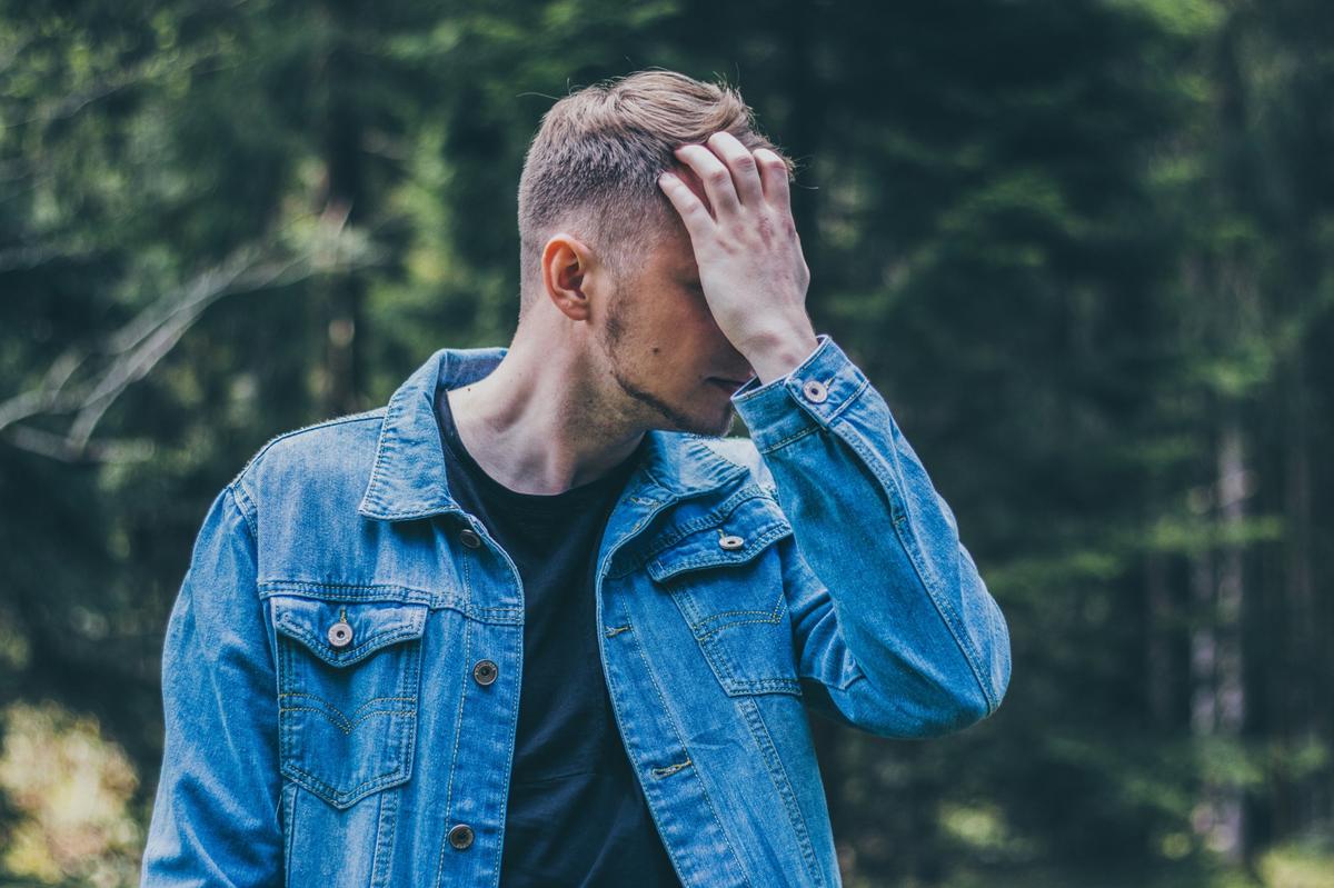 Man standing in nature holding his head, reflecting emotional overwhelm and mental health struggles, representing themes of therapy, counselling and self-reflection.
