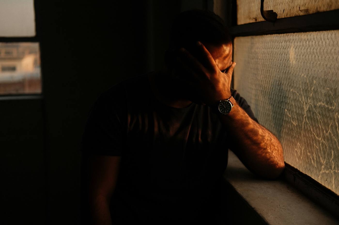 Man sitting alone by a window appearing distressed and emotionally overwhelmed, representing the psychological impact of emotional abuse, trauma, anxiety and mental health struggles.