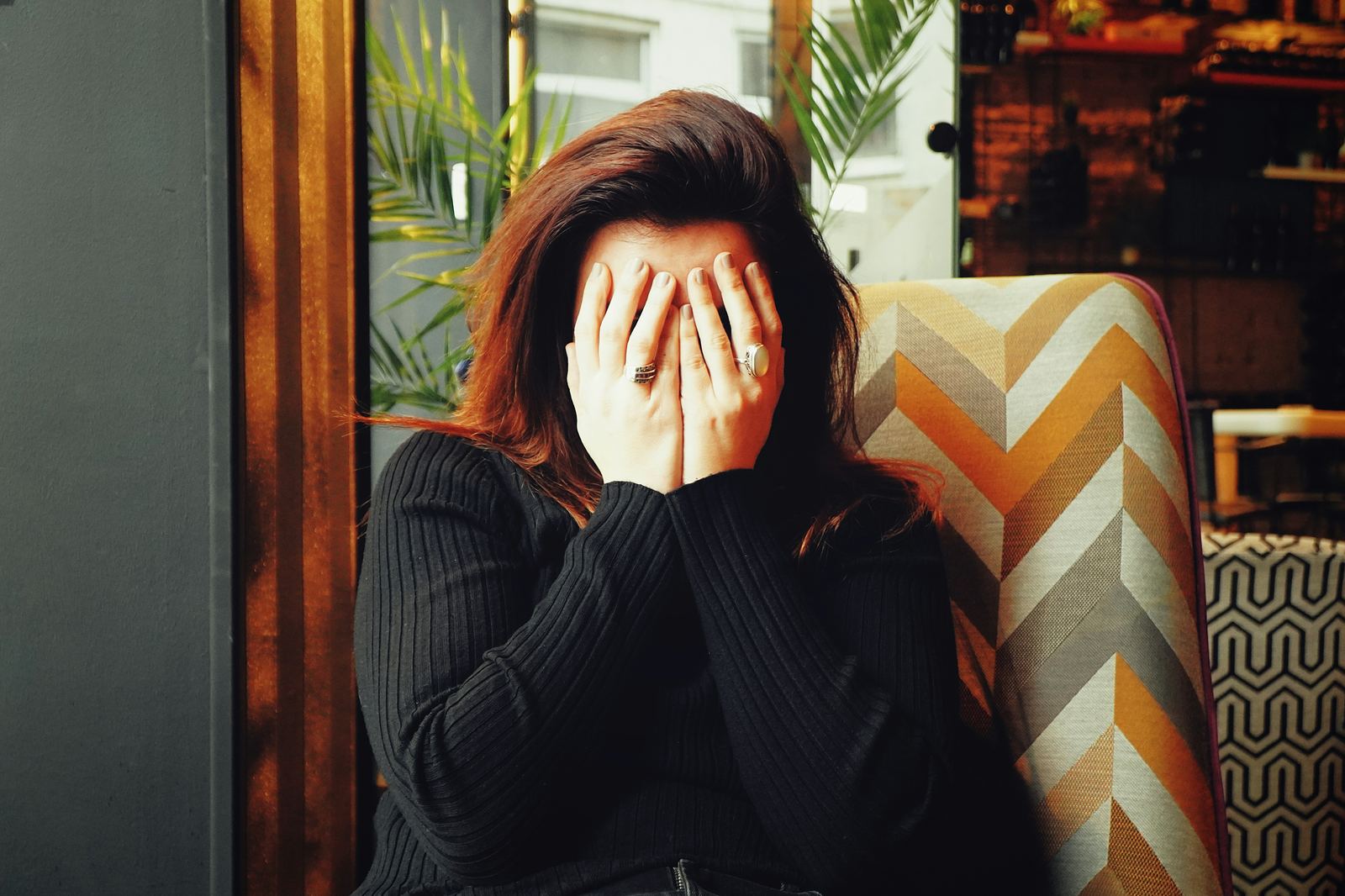 Woman sitting with her head in her hands, hiding her face in exhaustion, representing burnout, emotional overwhelm and the need for psychodynamic therapy support.