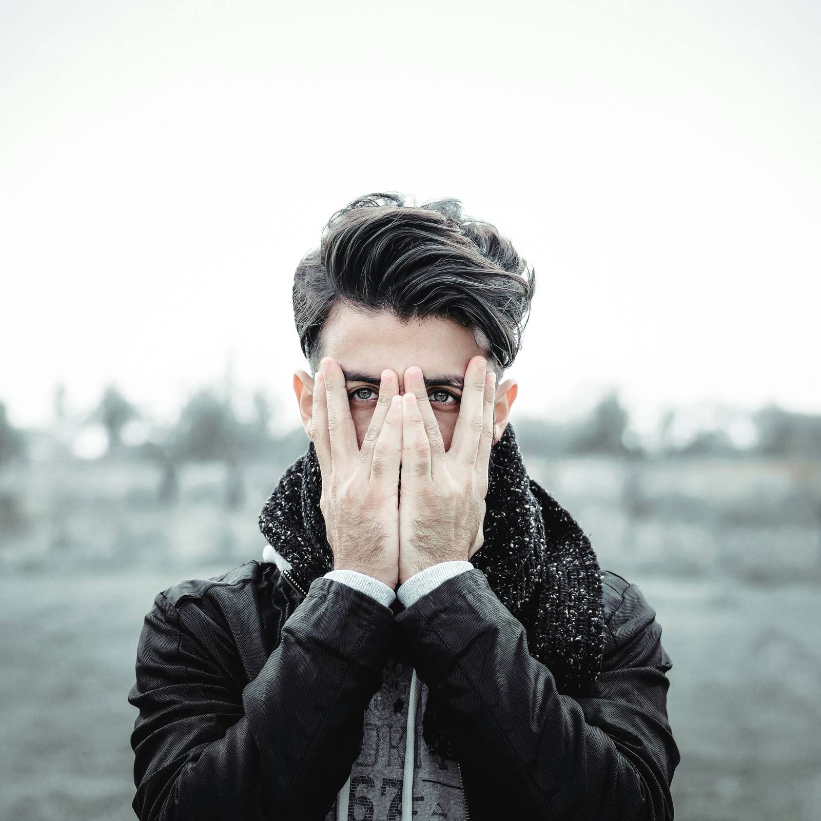 Man covering half his face with his hands, peering through his fingers, symbolising emotional overwhelm and the instinct to shut down or hide feelings — Serenity of Mind Therapy blog