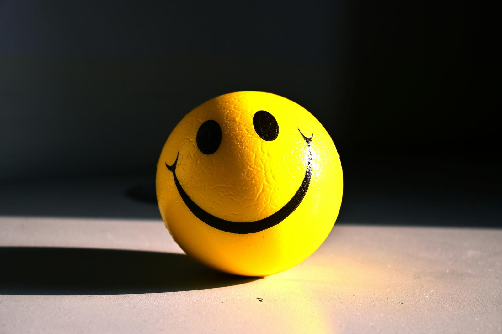 Bright yellow smiley face ball against a dark background, symbolising the performed cheerfulness behind people-pleasing — Serenity of Mind Therapy blog.