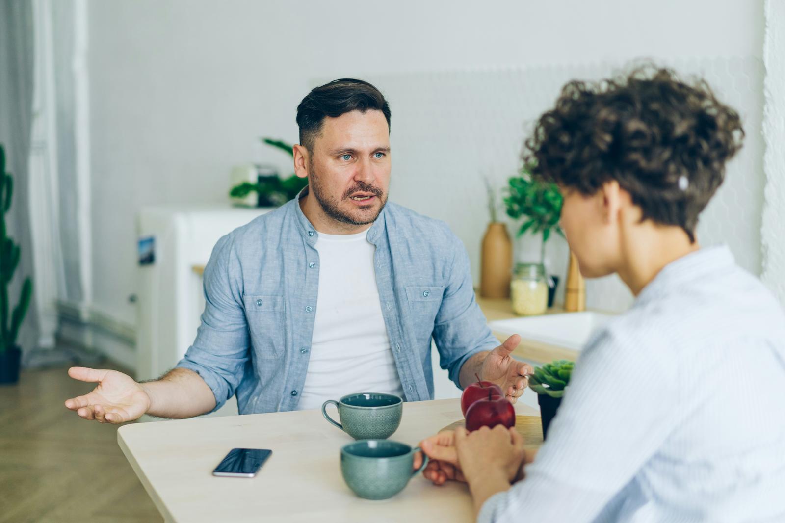 Couple having a tense but calm conversation at a kitchen table, illustrating the use of therapy language like "boundaries" in everyday relationships — Serenity of Mind Therapy blog