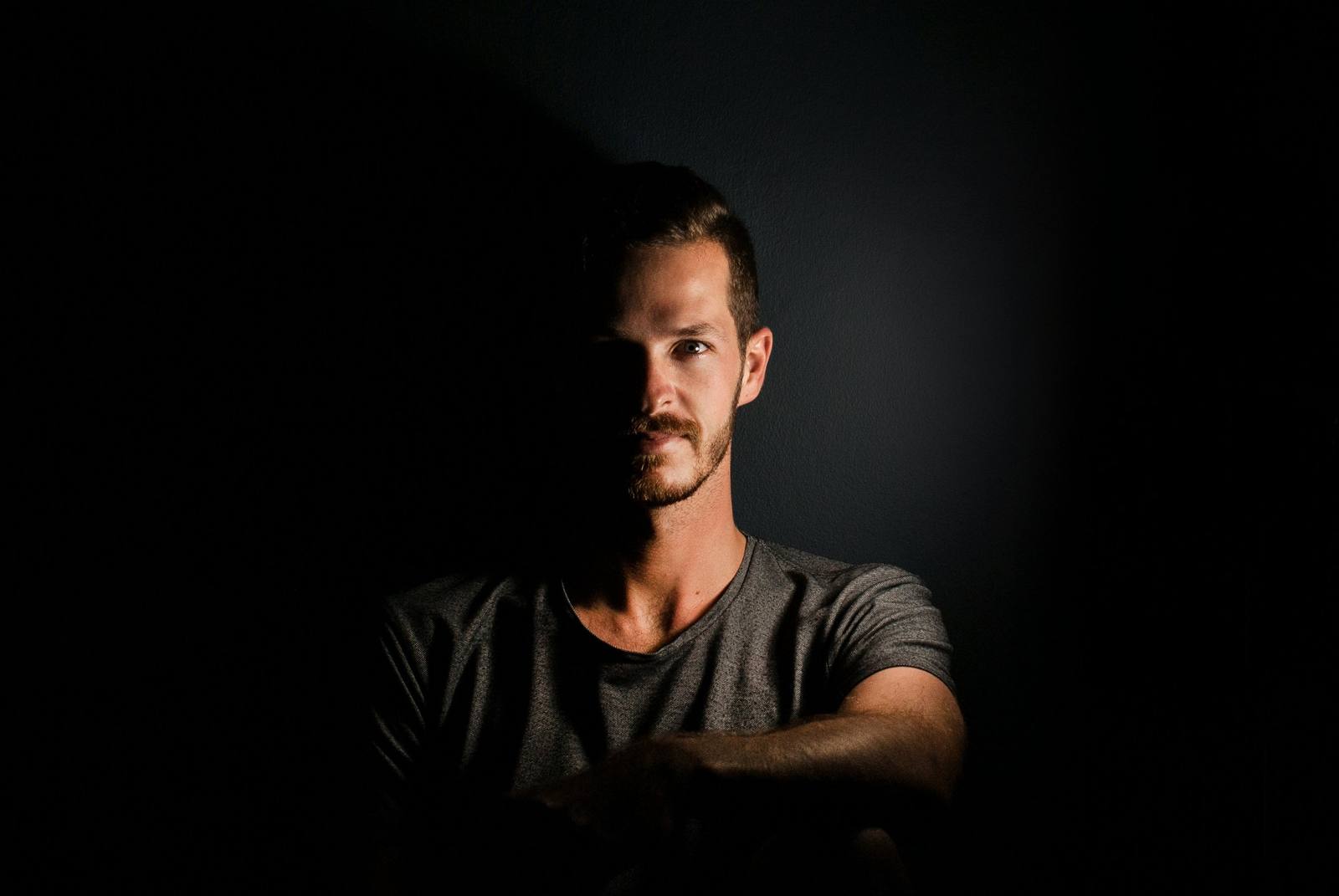 Man's face half-lit, half in shadow against a dark background, symbolising the hidden and visible parts of the self in relationships — Serenity of Mind Therapy blog
